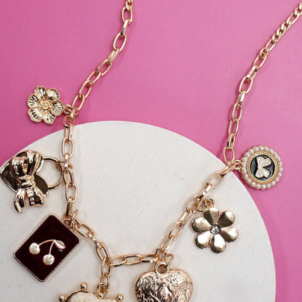 Gold charm necklace featuring bow, heart, cherry, and floral pendants on a link chain with extender clasp.