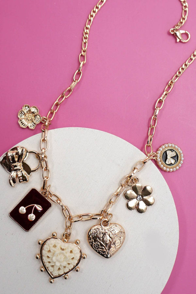 Gold charm necklace featuring bow, heart, cherry, and floral pendants on a link chain with extender clasp.