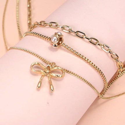 Layered gold necklace featuring delicate pearl strands and a small bow charm resting on a soft neutral background.