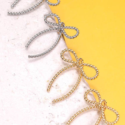 Bow-shaped earrings in gold and silver on a textured surface with a yellow background