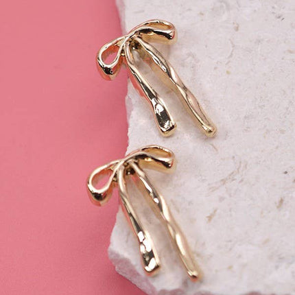 Gold bow-shaped earrings on a stone surface with a pink background