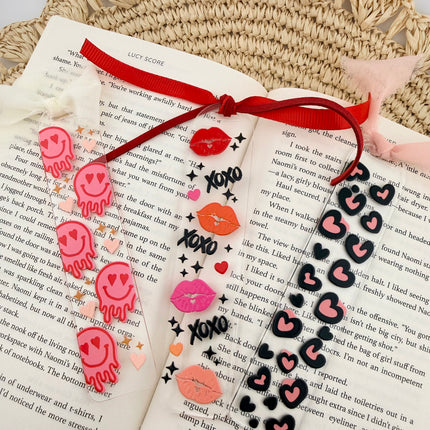 Clear acrylic Valentine’s Day bookmarks with pastel designs and soft chiffon ribbons resting inside open books, styled with a cozy, romantic bookish aesthetic.