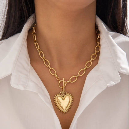 Gold chunky chain necklace with a front toggle clasp and oversized spiked heart pendant, worn on a model with a white blouse for a bold yet feminine statement look.