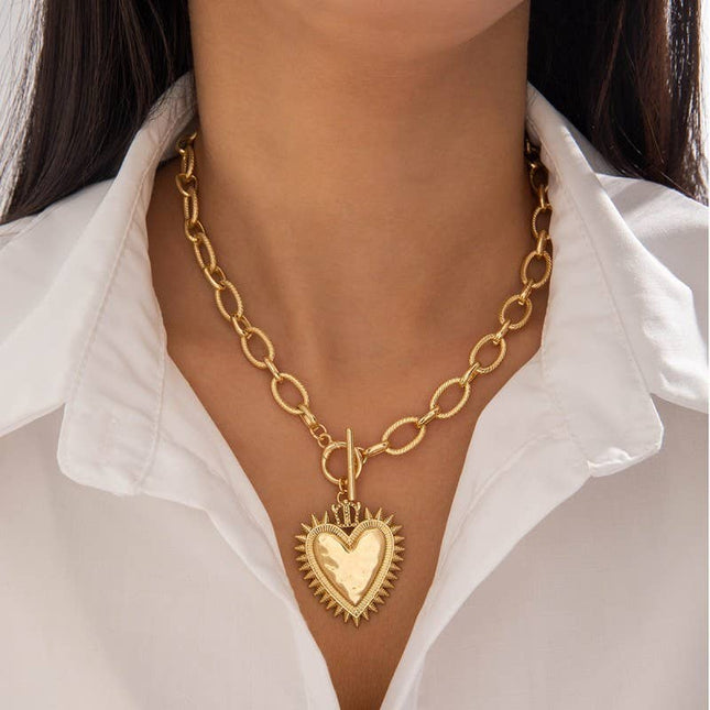 Gold chunky chain necklace with a front toggle clasp and oversized spiked heart pendant, worn on a model with a white blouse for a bold yet feminine statement look.