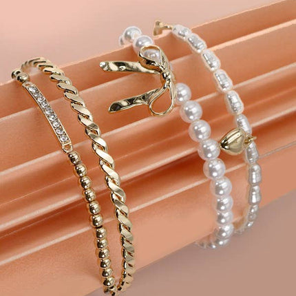 Set of 4 gold and pearl stretch bracelets with bow charm, rhinestone bar, and gold beading on soft green display.