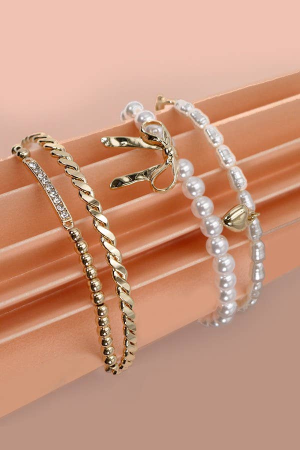 Set of 4 gold and pearl stretch bracelets with bow charm, rhinestone bar, and gold beading on soft green display.