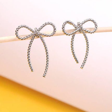 Bow-shaped earrings on a white stick with a yellow background