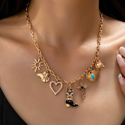 Gold paperclip chain necklace with western-inspired charms including a cowboy boot, heart, cross, sunburst, and hat, styled on a model’s neckline against a soft neutral background