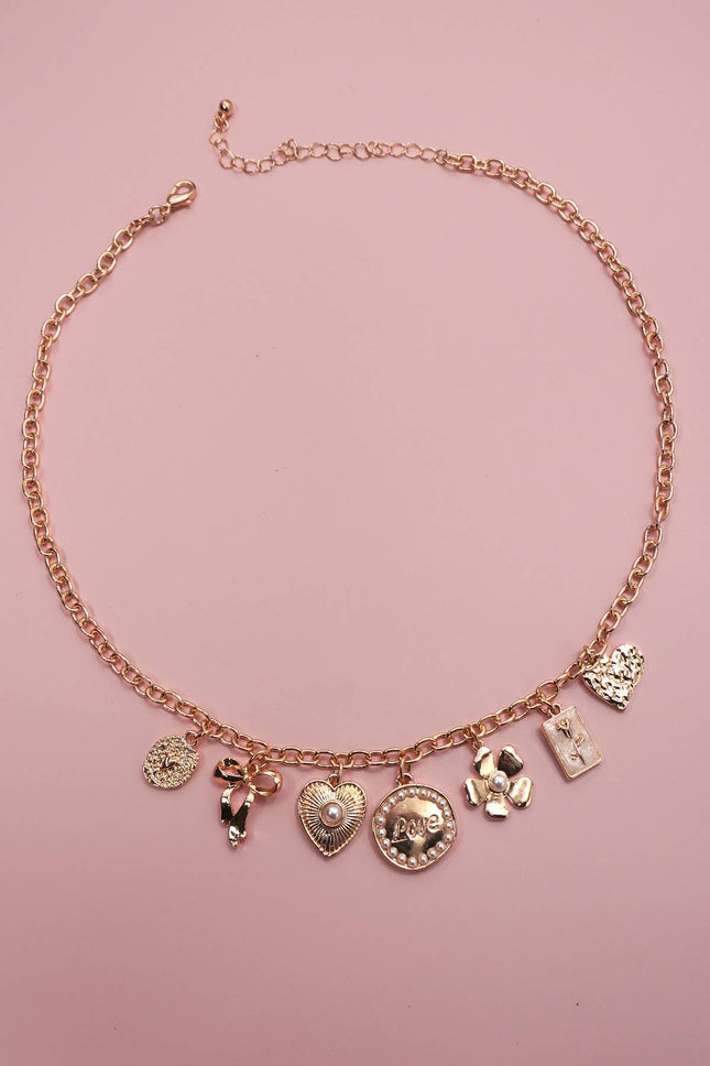 Rose gold necklace with various charms on a pink background