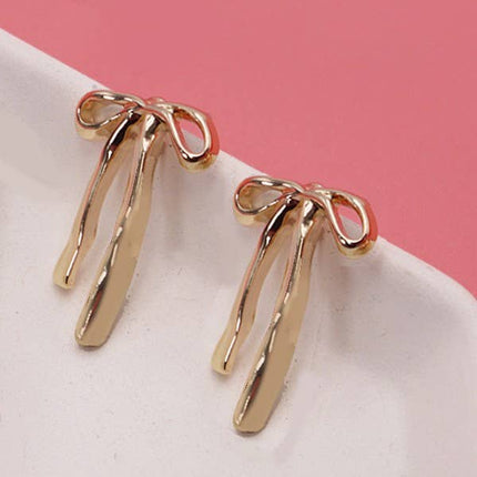 Gold earrings on a white surface with a pink background