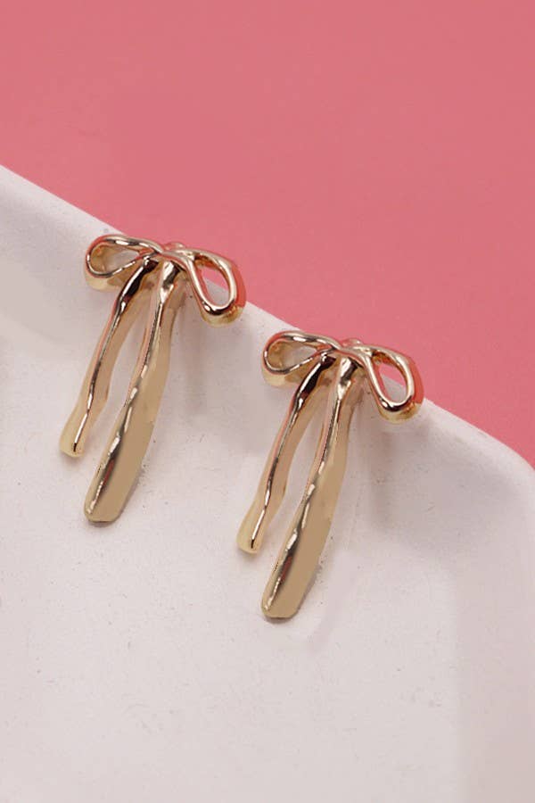 Gold earrings on a white surface with a pink background