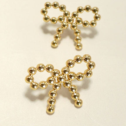 Gold bow-shaped earrings on a beige background
