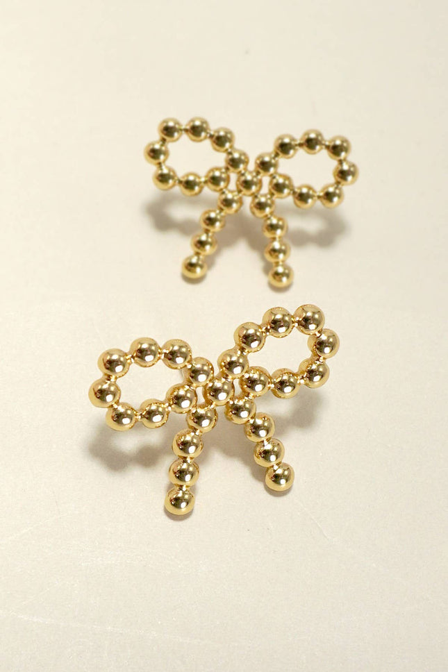 Gold bow-shaped earrings on a beige background