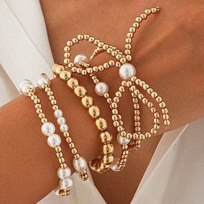 Gold multi-layer stretch bracelet featuring pearl beads, ball chain details, and a bow charm styled on a wrist.