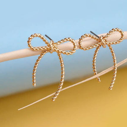 Gold bow-shaped earrings on a stick against a blue and yellow gradient background