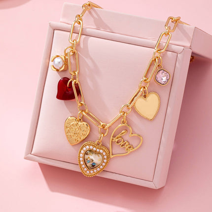 Gold plated elongated paperclip chain necklace with dangling porcelain heart, rhinestone crystal, pearl cluster, and red enamel heart charms styled in a romantic feminine jewelry aesthetic.