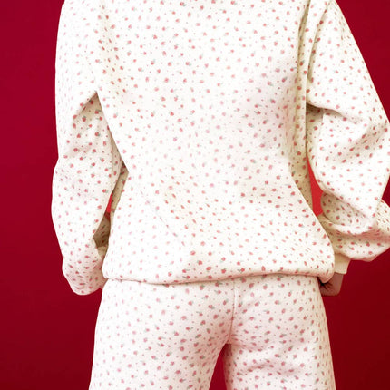 Model wearing a pink floral hoodie with a kangaroo pocket and matching sweatpants styled in a relaxed fit against a red background.