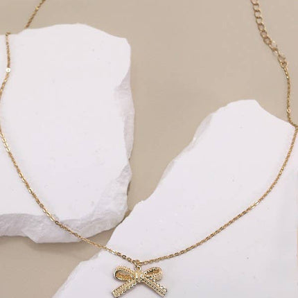 Gold necklace with a bow pendant on a white stand against a beige background