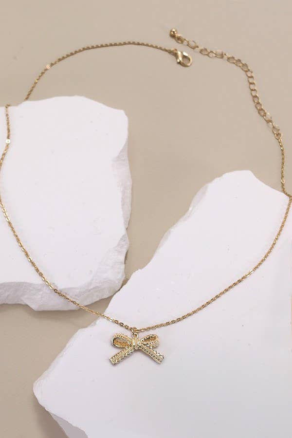 Gold necklace with a bow pendant on a white stand against a beige background