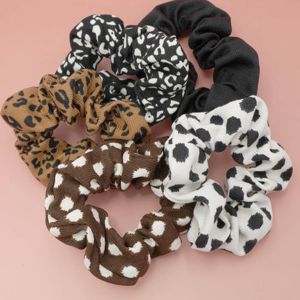 Set of five animal pattern scrunchies in mixed neutral prints displayed on a soft blush background, highlighting their stretchy, soft polyester fabric and assorted designs.