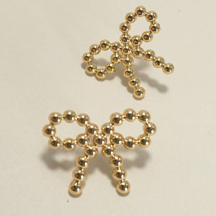 Gold bow-shaped jewelry on a beige background