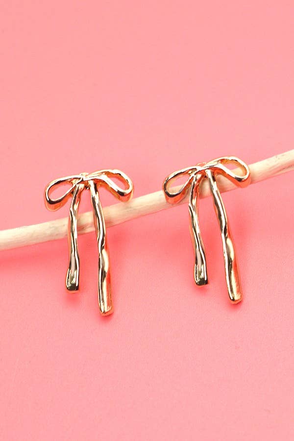 Gold bow-shaped earrings on a pink background