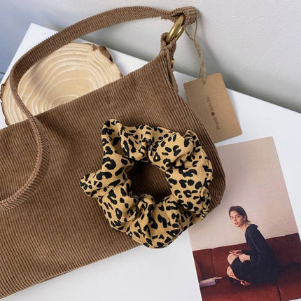 Brown handbag with a leopard print scrunchie on a white surface