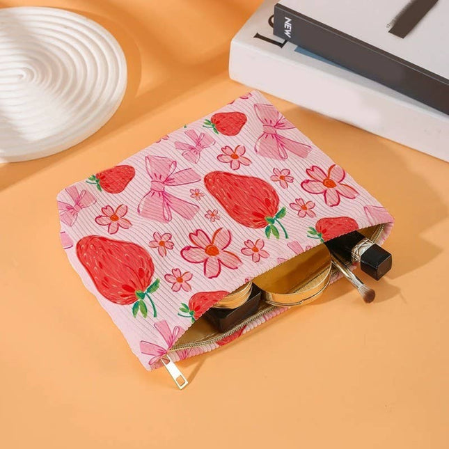 Floral and strawberry-patterned pouch with makeup items on a peach-colored surface