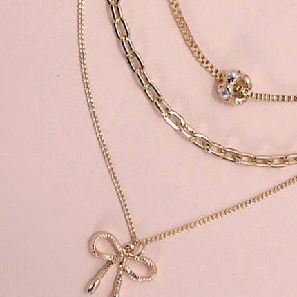Layered gold necklace featuring delicate pearl strands and a small bow charm resting on a soft neutral background.