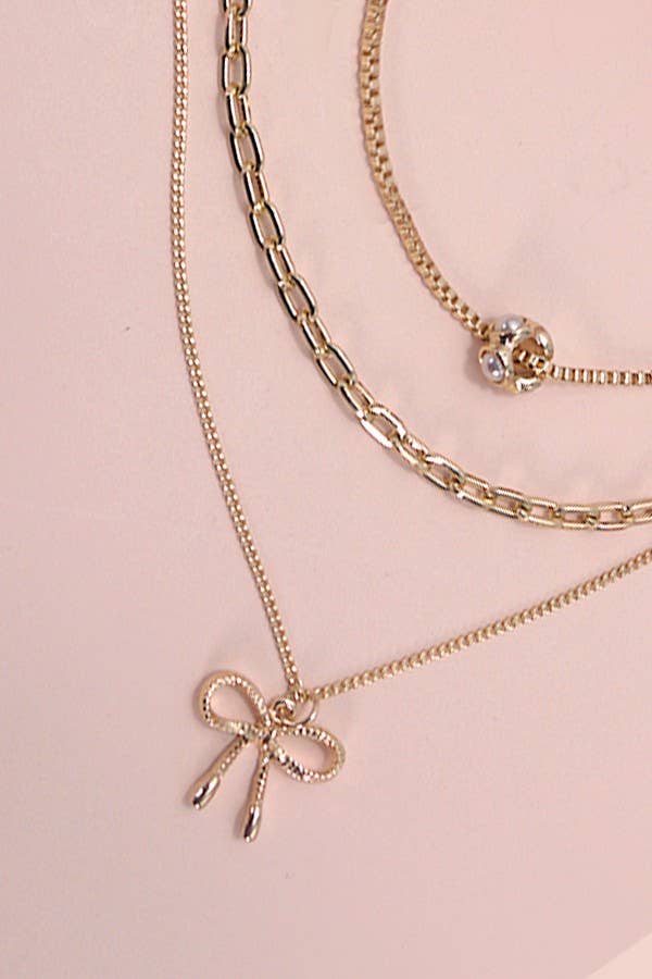 Layered gold necklace featuring delicate pearl strands and a small bow charm resting on a soft neutral background.
