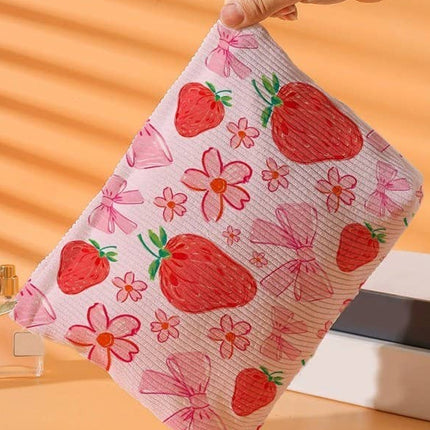 Hand holding a pink towel with strawberry pattern against an orange background