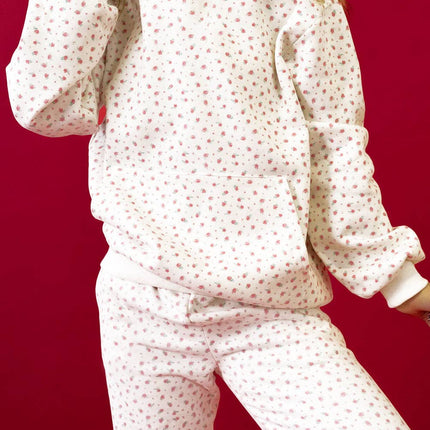 Model wearing a pink floral hoodie with a kangaroo pocket and matching sweatpants styled in a relaxed fit against a red background.