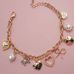 Gold-plated charm bracelet with bow, heart, pearl, and textured disc charms, 6.5” with 2” adjustable extender