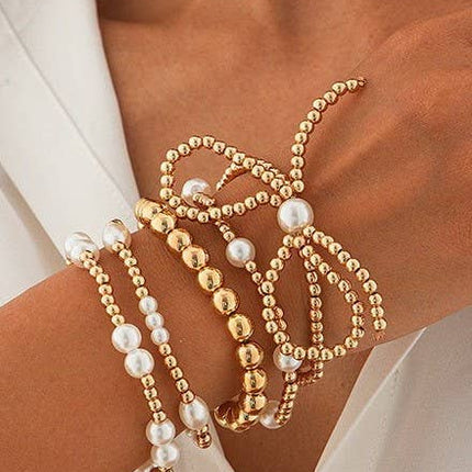 Gold multi-layer stretch bracelet featuring pearl beads, ball chain details, and a bow charm styled on a wrist.