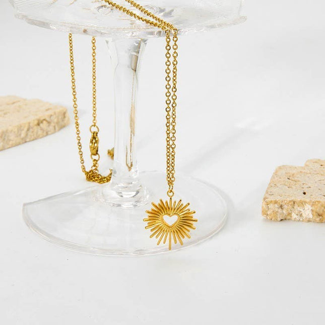 Gold necklace with a sunflower pendant on a clear stand against a white background