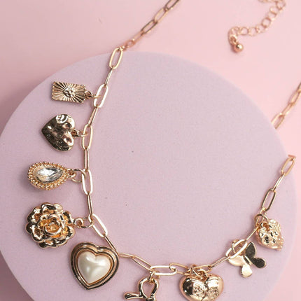 Gold necklace with various charms on a pink background