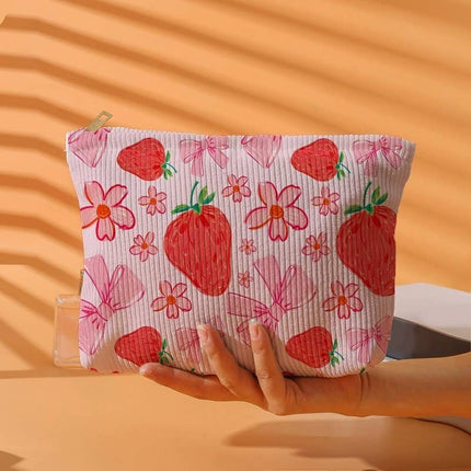 Hand holding a pouch with strawberry and flower pattern against an orange background