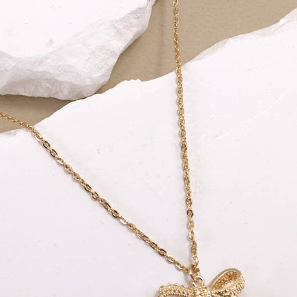 Gold necklace with a bow pendant on a white surface