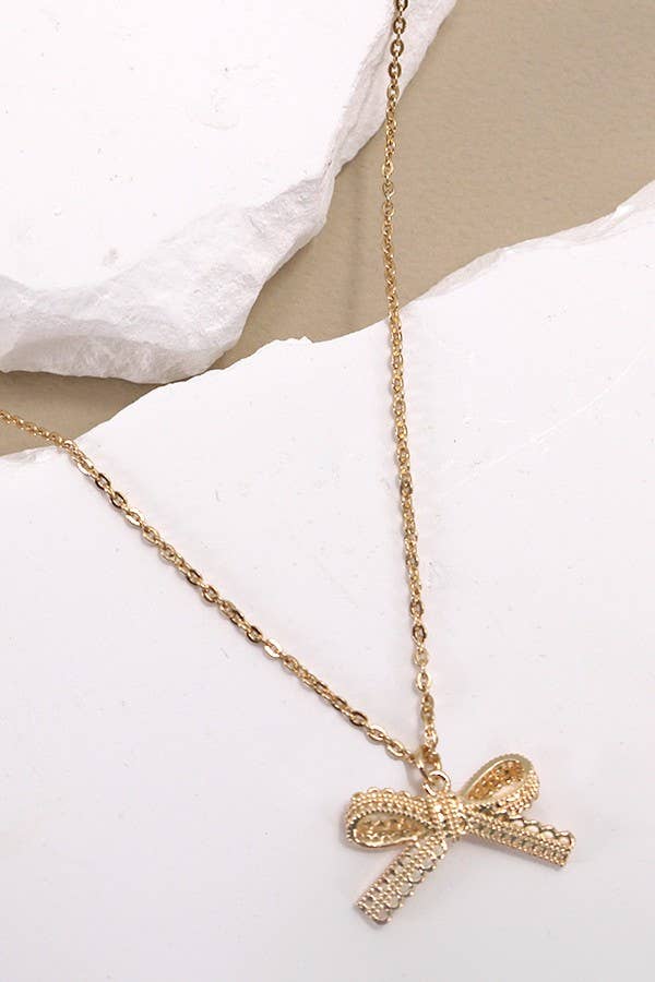 Gold necklace with a bow pendant on a white surface