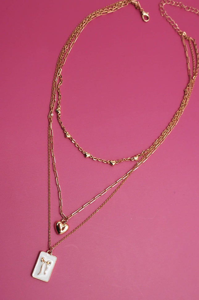 Gold necklaces with heart and rectangular pendants on a pink background