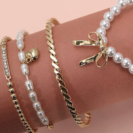 Set of 4 gold and pearl stretch bracelets with bow charm, rhinestone bar, and gold beading on soft green display.