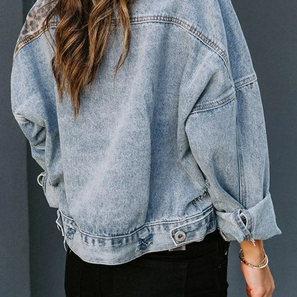 Model wearing a distressed blue denim jacket with leopard print patchwork panels, styled casually over a black top with layered necklaces.