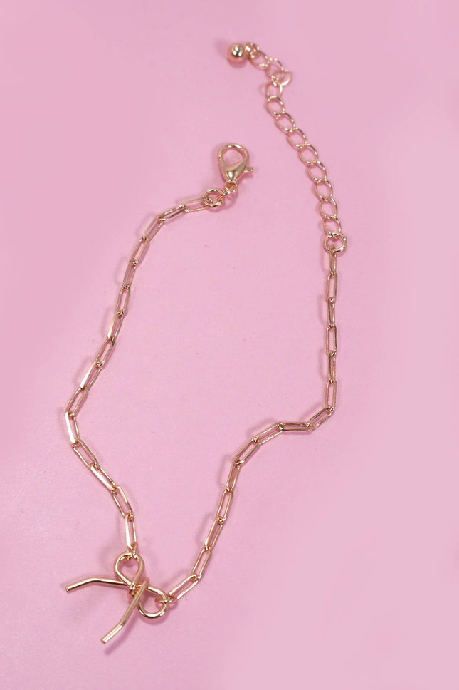 Gold chain bracelet with a small charm on a pink background