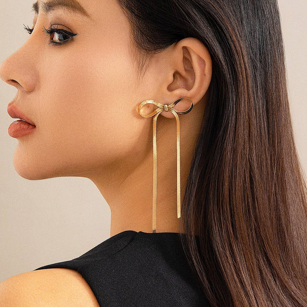 Gold bow-shaped earrings worn by a model on a beige background
