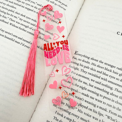 Handmade acrylic Valentine’s Day bookmarks featuring pink and red heart-themed designs with tassels, styled on open books for a cozy, festive reading aesthetic.