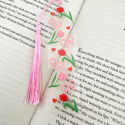 Handmade acrylic Valentine’s Day bookmarks featuring pink and red heart-themed designs with tassels, styled on open books for a cozy, festive reading aesthetic.