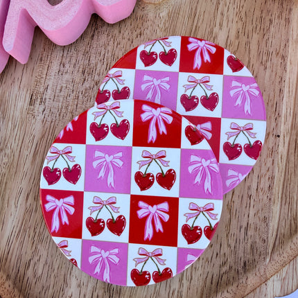 Round ceramic Valentine coasters featuring pink and red heart, bow, and XOXO designs, styled on a neutral surface and packaged ready to gift.
