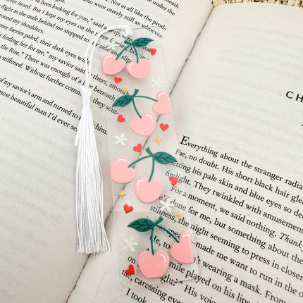 Handmade acrylic Valentine’s Day bookmarks featuring pink and red heart-themed designs with tassels, styled on open books for a cozy, festive reading aesthetic.