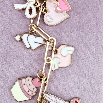 Valentine’s-themed charm keychain featuring pink and red enamel heart and love charms clipped to a phone case and displayed on a soft pink background.
