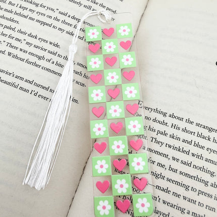 Handmade acrylic Valentine’s Day bookmarks featuring pink and red heart-themed designs with tassels, styled on open books for a cozy, festive reading aesthetic.